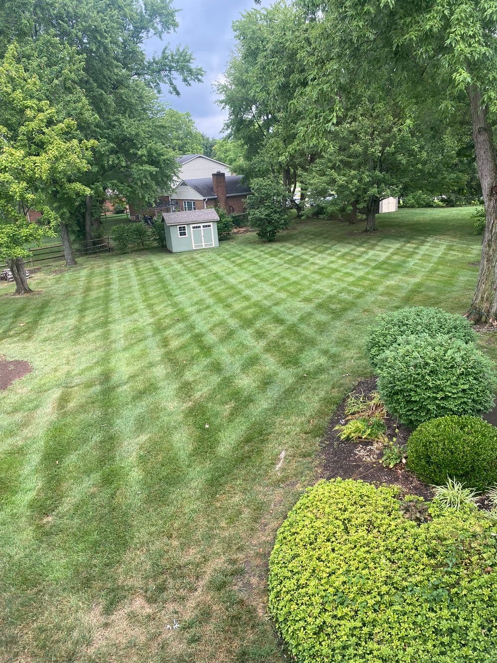 Lush green lawn with striped patterns and landscaped shrubs under a cloudy sky.