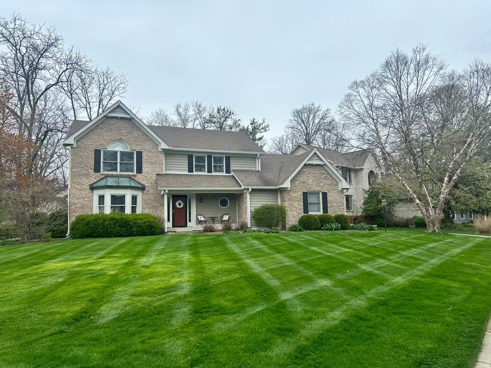 Spacious brick house with manicured lawn and neat landscaping on a cloudy day.