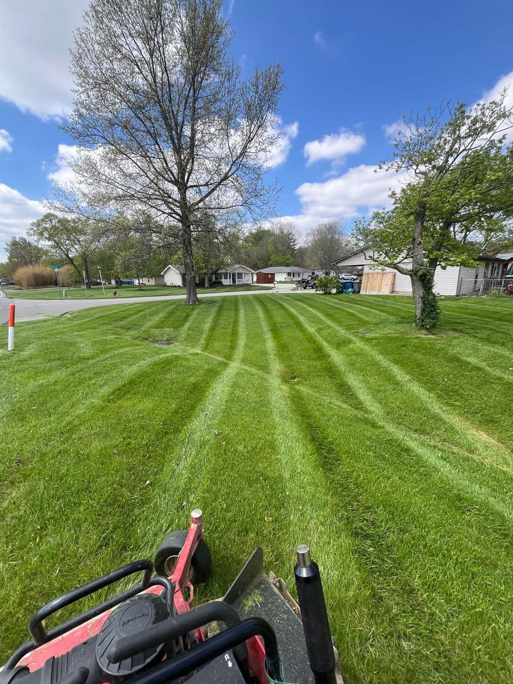 Lawn mower in foreground with freshly mowed grass and suburban homes under a blue sky.