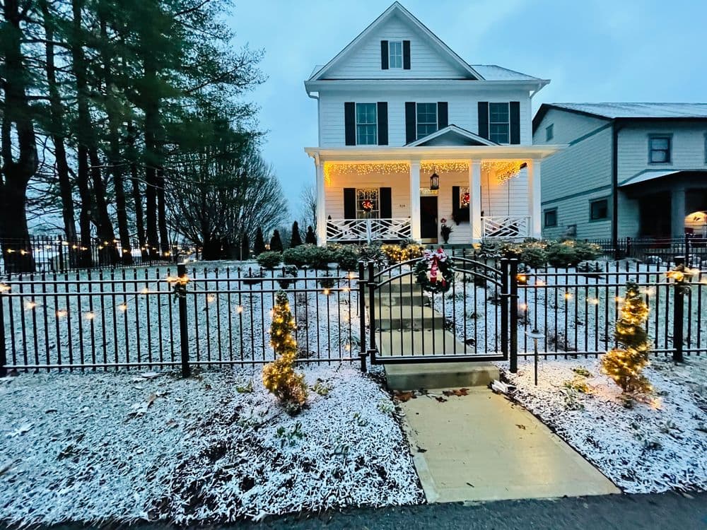 Charming neighborhood house adorned with festive lights and snowy landscape.